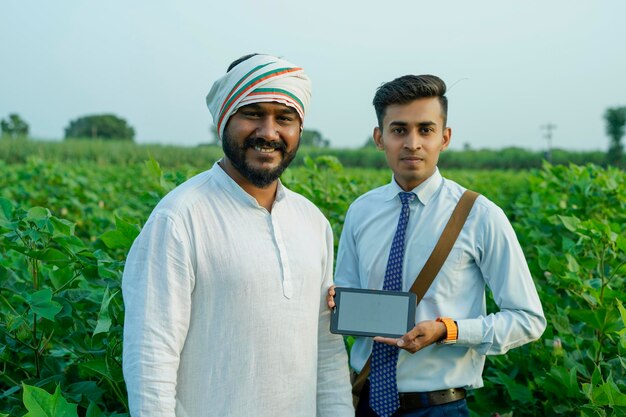 Foto un giovane agronomo indiano mostra alcune informazioni a un contadino su un tablet in un campo agricolo