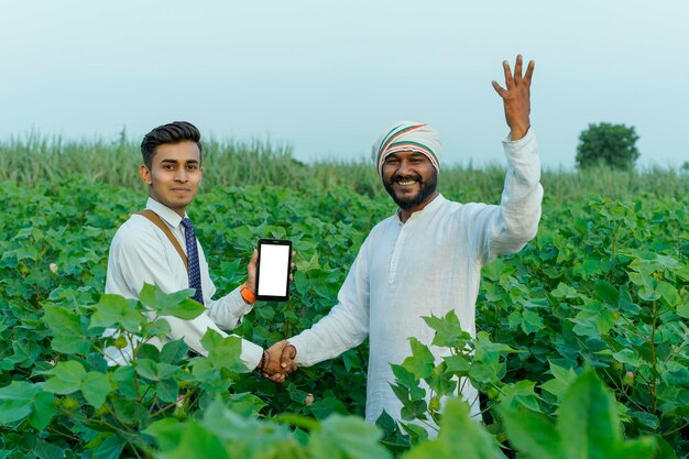 Foto un giovane agronomo indiano mostra alcune informazioni a un contadino su un tablet in un campo agricolo