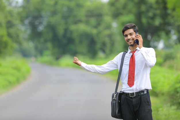Young indian agronomist using smart phone on road side and asking lift