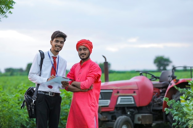 Young indian bank officer showing detail of loan paper to farmer at field