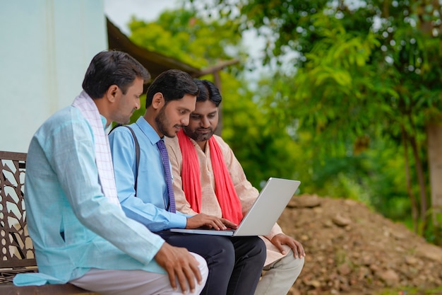 Young indian banker or agronomist showing some detail to farmers in laptop at home