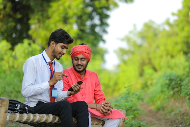 Young indian banker discuss with farmer at field