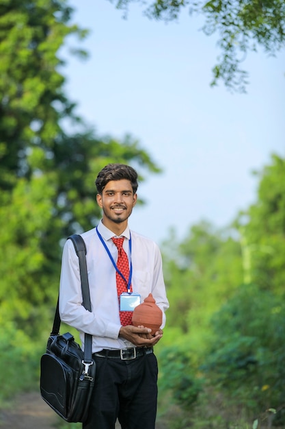 Young indian banker holding clay piggy bank in hand