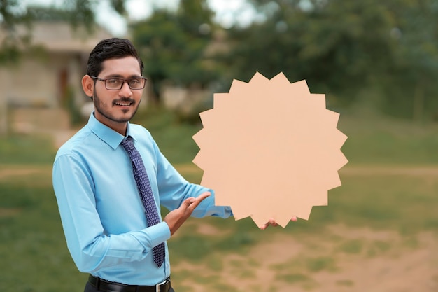 Молодой индийский банкир или офицер показывая пустую доску на фоне природы.