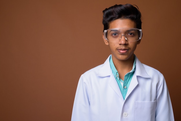 Young Indian boy doctor wearing protective glasses against brown background