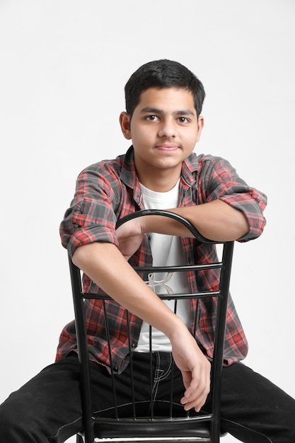 Young indian boy sitting on chair and showing expression on white wall