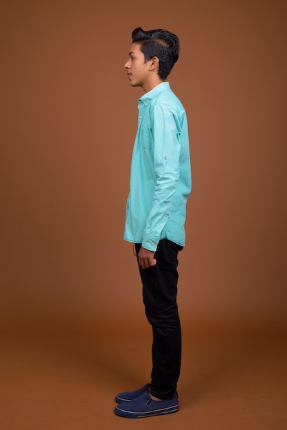 Young Indian boy wearing blue shirt looking smart against brown background