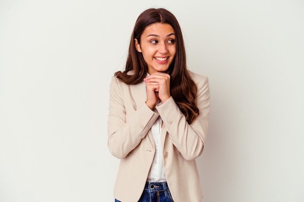 Young Indian business woman isolated on white wall keeps hands under chin, is looking happily aside.