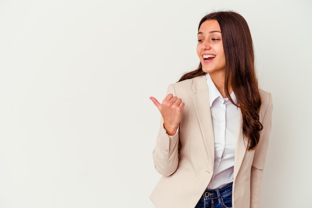 Young Indian business woman isolated on white wall points with thumb finger away, laughing and carefree.