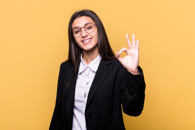 Young Indian business woman isolated on yellow wall cheerful and confident showing ok gesture