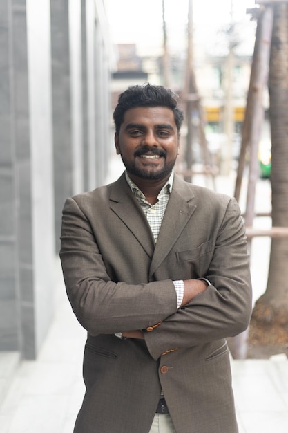 Young Indian businessman smiling portrait on the way to his office against contemporary corporate buildings in the city