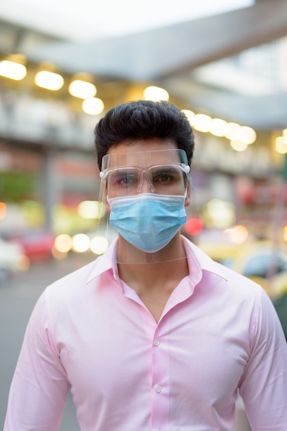 Young Indian businessman wearing mask and face shield in the city streets outdoors