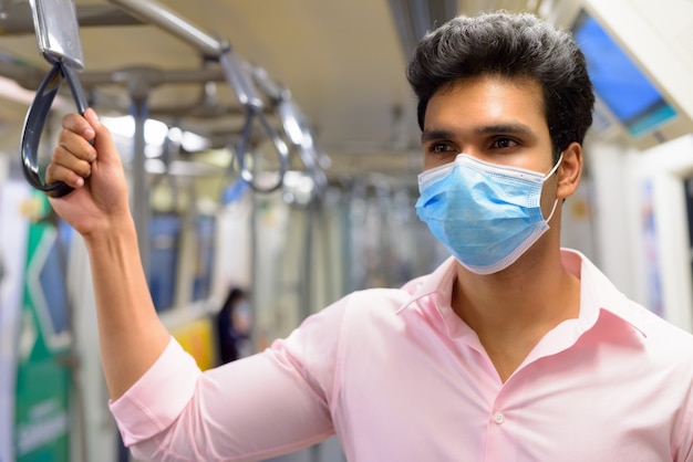 Young Indian businessman wearing mask and standing with distance inside the train