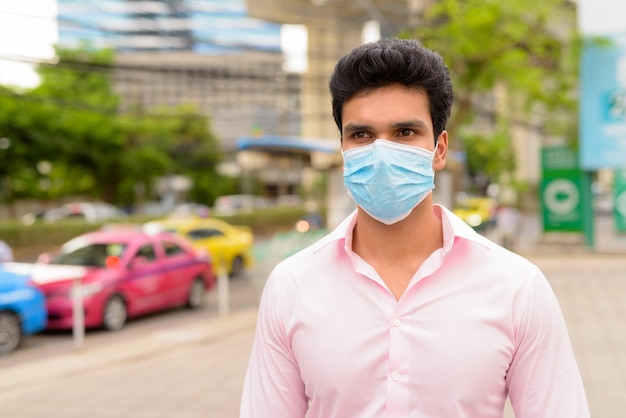 Young Indian businessman with mask waiting at taxi station in the city