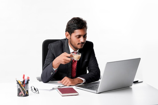 Молодой индийский бизнесмен работает на ноутбуке и пьет чай в офисе.