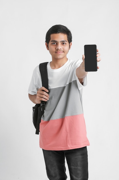 Young indian college student showing smartphone screen on white wall