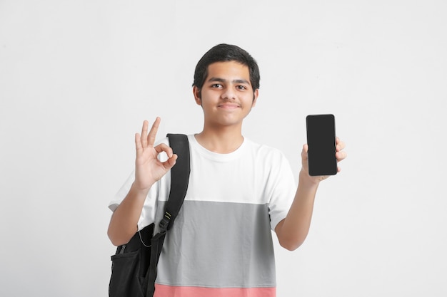 Young indian college student showing smartphone screen on white wall