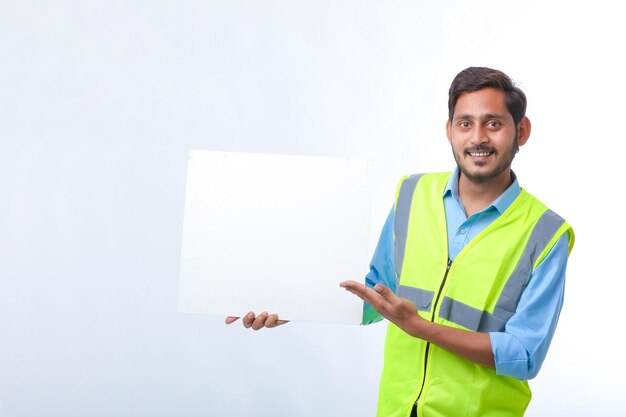 Young indian Construction Worker Showing Empty Poster Board on White Background.