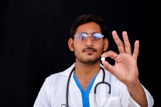 Young indian doctor holding pill in hand.