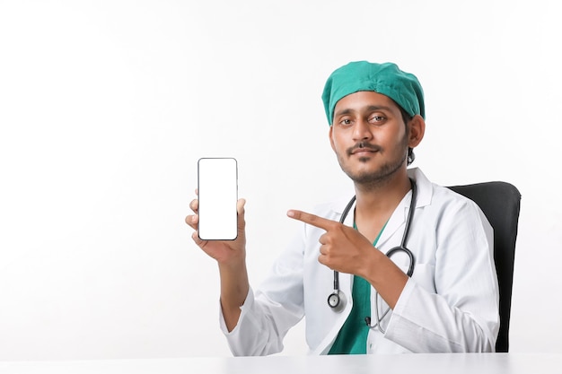 흰색 배경 위에 스마트폰 화면을 보여주는 젊은 인도 의사.