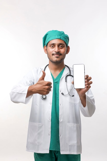 白い背景の上にスマートフォンの画面を表示している若いインドの医師。