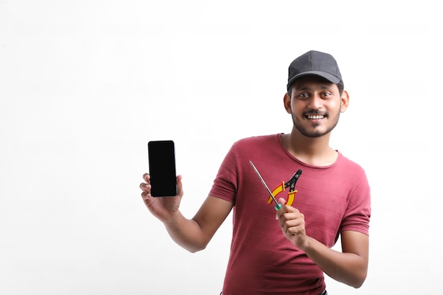 Young indian electrician holding tools in hand and showing smartphone.