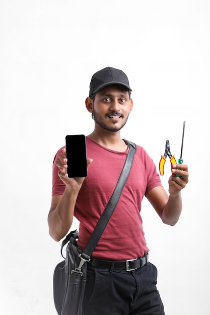 Young indian electrician holding tools in hand and showing smartphone.