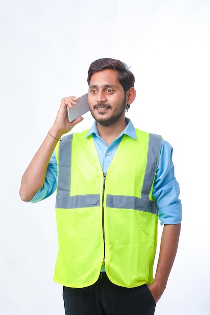 Young indian engineer wearing hardhat and talking smartphone on white background.