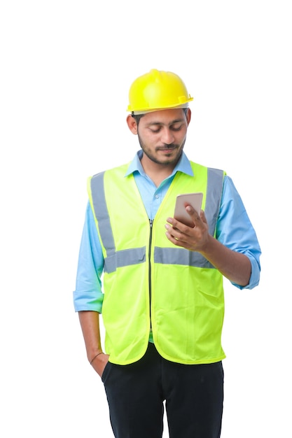 Young indian engineer wearing hardhat and using smartphone on white background.