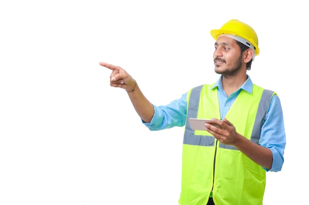 Young indian engineer wearing hardhat and using smartphone on white background.