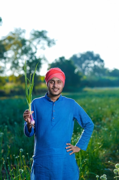 Young indian farmer holding onion crop in hand at agriculture field