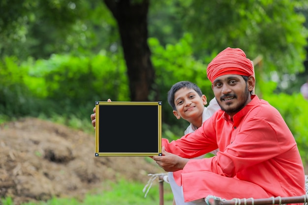 Young indian farmer showing blank chalkboard with his child