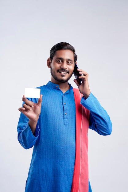 Young indian farmer showing card and talking on mobile phone over white background