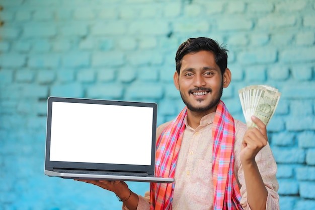 Young indian farmer showing laptop screen and money