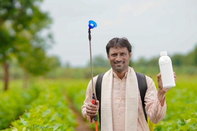 Young indian farmer showing liquid fertilizer bottle at agriculture field.