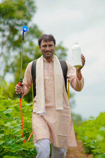 Young indian farmer showing liquid fertilizer bottle at agriculture field.