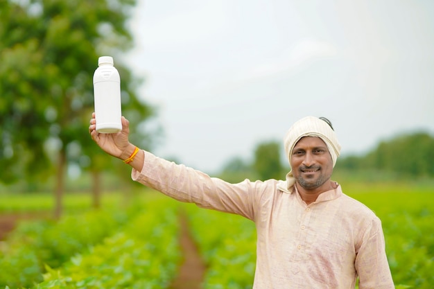 Young indian farmer showing liquid fertilizer bottle at agriculture field.