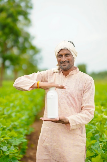 Young indian farmer showing liquid fertilizer bottle at agriculture field.