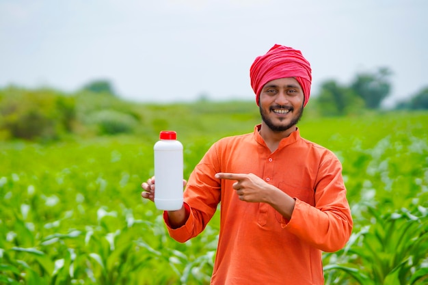 Young indian farmer showing liquid fertilizer bottle at\
agriculture field.