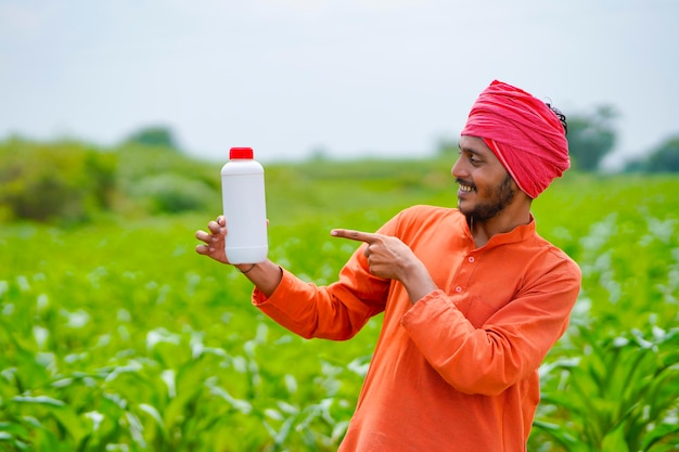 Young indian farmer showing liquid fertilizer bottle at agriculture field.