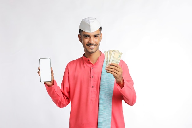 白い背景の上のスマートフォンとお金を示す若いインドの農家。