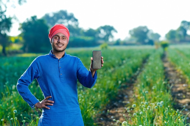 Young indian farmer showing smartphone screen at agriculture field