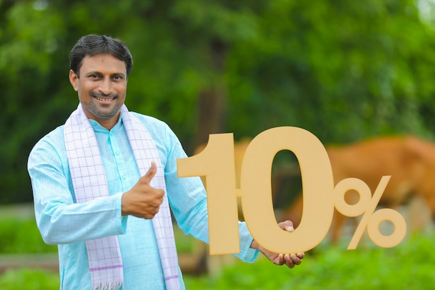 Young indian farmer showing ten percent board at his farm