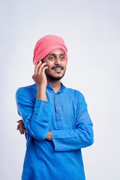 白い背景の上の携帯電話で話している若いインドの農夫。
