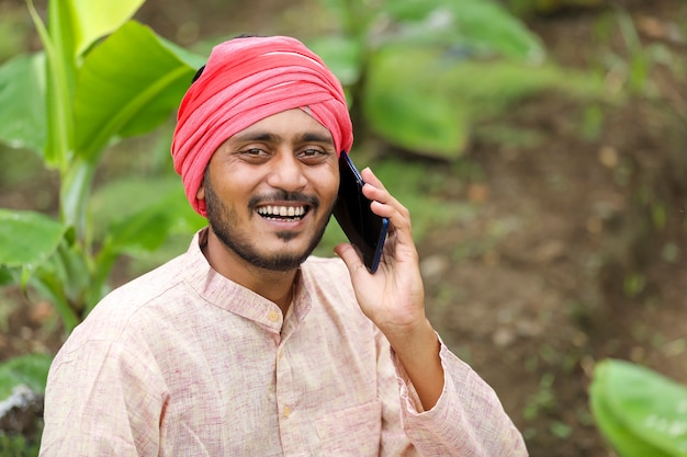 Young indian farmer talking on smartphone at banana agriculture field.