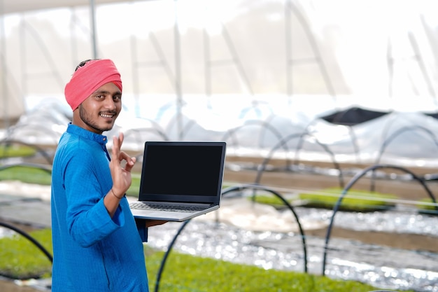 온실 또는 폴리 하우스에서 노트북을 사용하는 젊은 인도 농부