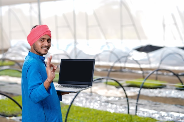 Young indian farmer using laptop at greenhouse or poly house