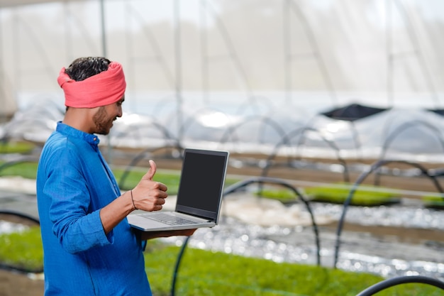 Giovane agricoltore indiano utilizzando laptop in serra o poli casa