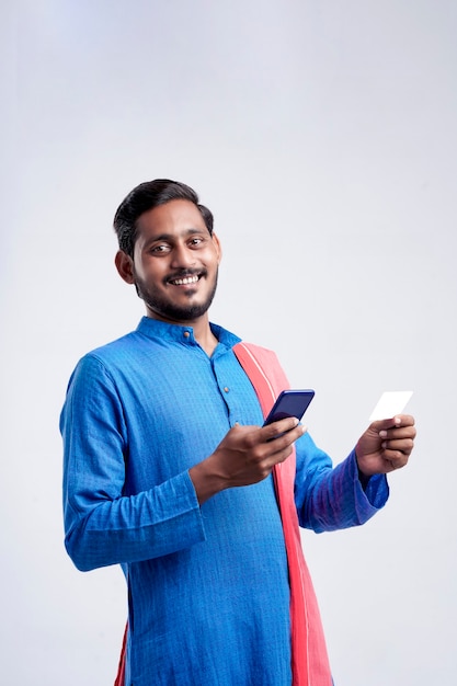 Молодой индийский фермер с помощью смартфона и банковской карты на белом фоне.