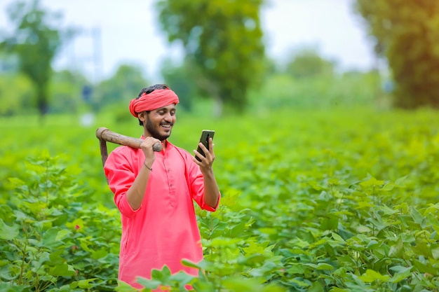 緑の綿花畑でスマートフォンを使用して若いインドの農民